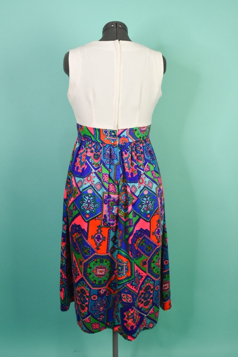 May include: A white sleeveless dress with a colorful geometric print skirt. The skirt features a mix of blue, green, pink, and orange colors.