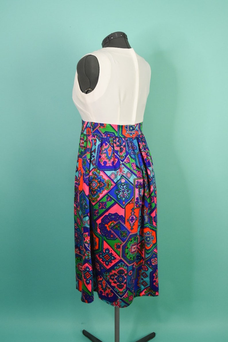 May include: A white sleeveless dress with a colorful geometric print skirt. The skirt is made of a patterned fabric with shades of blue, green, pink, and orange.