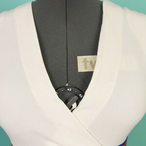 May include: White wrap dress with a colorful paisley print skirt. The dress has a V-neckline and a fitted bodice.