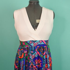 May include: A white sleeveless dress with a V-neckline and a colorful geometric print skirt. The skirt features a variety of colors, including blue, green, pink, and orange.
