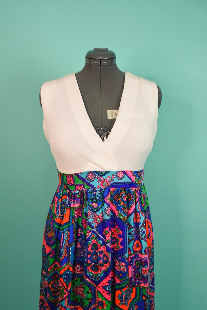 May include: A white sleeveless dress with a V-neckline and a colorful geometric print skirt. The skirt features a variety of colors, including blue, green, pink, and orange.