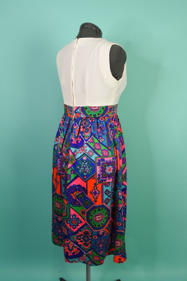 May include: A white sleeveless dress with a colorful geometric print skirt. The skirt features a variety of colors, including blue, green, pink, and orange.