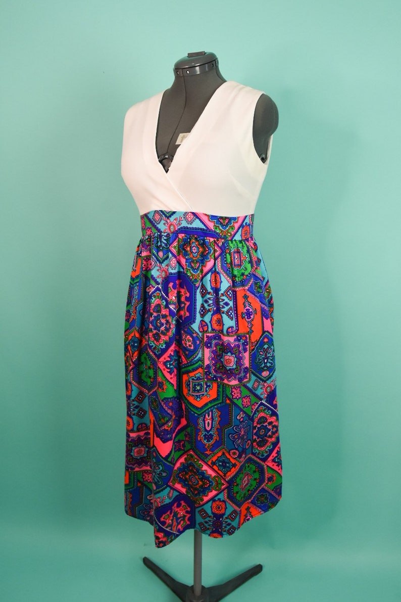 May include: A white sleeveless dress with a geometric print skirt. The skirt is a mix of blue, green, pink, and orange colors.