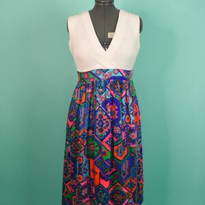 May include: A white sleeveless dress with a V-neckline and a colorful geometric print skirt. The skirt is made of a patterned fabric with shades of blue, pink, green, and orange.