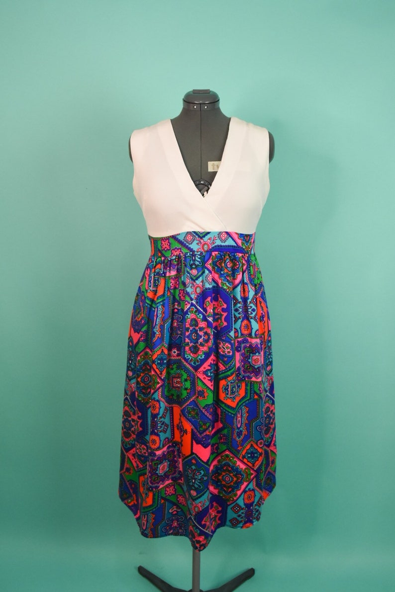 May include: A white sleeveless dress with a V-neckline and a colorful geometric print skirt. The skirt is made of a patterned fabric with shades of blue, pink, green, and orange.