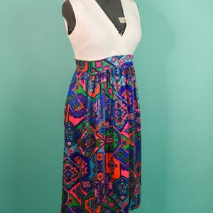 May include: A white sleeveless dress with a V-neckline and a colorful geometric print skirt. The skirt is made of a patterned fabric with shades of blue, pink, green, and orange.