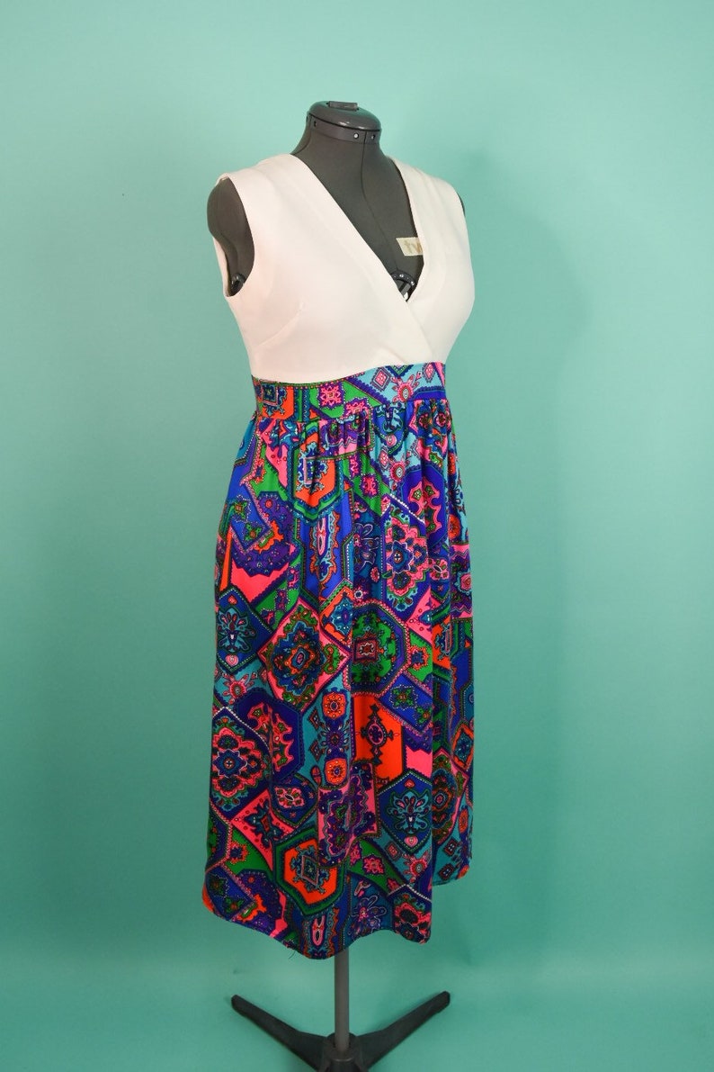 May include: A white sleeveless dress with a V-neckline and a colorful geometric print skirt. The skirt is made of a patterned fabric with shades of blue, pink, green, and orange.