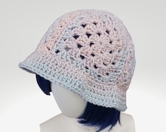 May include: A crocheted bucket hat with a light blue and pink ombre color pattern. The hat is made with a delicate open stitch design.
