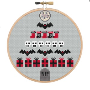 May include: Cross-stitch design in a wooden hoop featuring a gray background with a Christmas tree made of skulls, bats, and presents. The tree is topped with a clock and a bat. The bottom has a tombstone with "RIP".