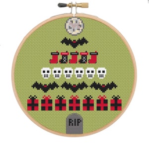 May include: Cross-stitch embroidery in a wooden hoop features a Halloween-themed Christmas tree design. The tree is composed of bats, skulls, stockings, and presents in red, black, and white against a green background. A tombstone with "RIP" is at the base.