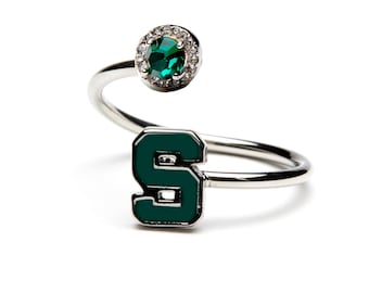 May include: A silver ring with a green letter 'S' and a green gemstone surrounded by clear rhinestones.