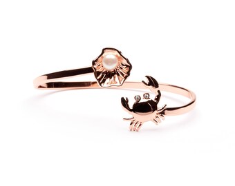 May include: A rose gold bracelet with a shell and a crab charm. The shell has a pearl in the center.