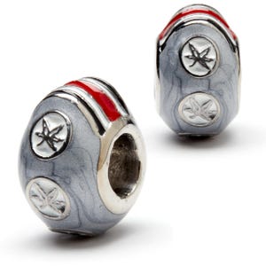 May include: A silver charm bead with a gray and white marbled design. The bead has a red stripe and two white stars with a red outline.