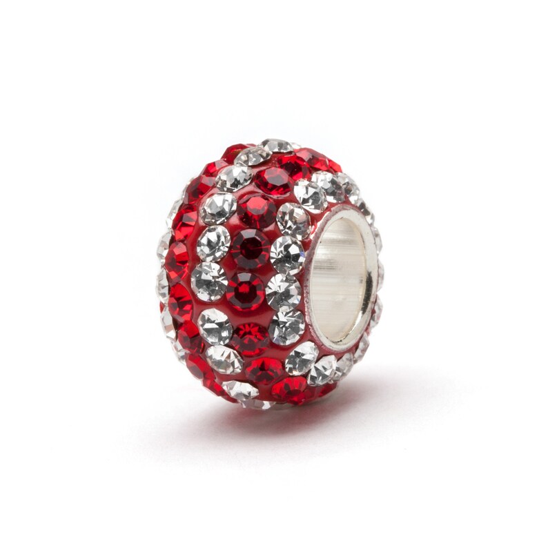 Puede incluir: Un abalorio de cristal rojo y transparente con un anillo de metal plateado. La cuenta est&aacute; cubierta de peque&ntilde;os cristales rojos y transparentes.