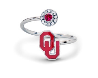 May include: A silver ring with a red and white OU logo and a red stone surrounded by clear stones.