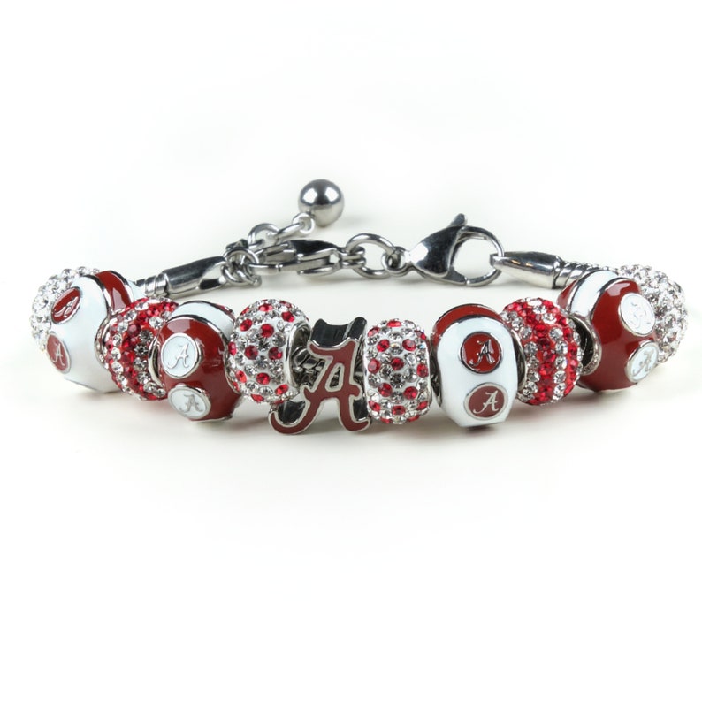 Puede incluir: Un brazalete de plata con abalorios rojos y blancos y un abalorio rojo y blanco con la letra 'A' en letra cursiva. Los abalorios est&aacute;n decorados con pedrer&iacute;a transparente.