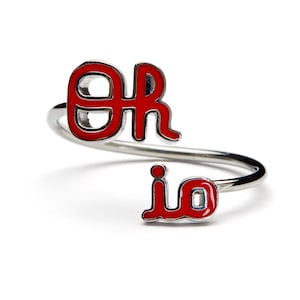 May include: A silver ring with red enamel letters spelling "or" and "io".