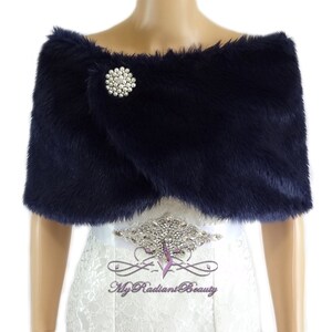 May include: Navy blue faux fur shawl with a jeweled brooch. The shawl is draped over a white dress with a beaded belt.