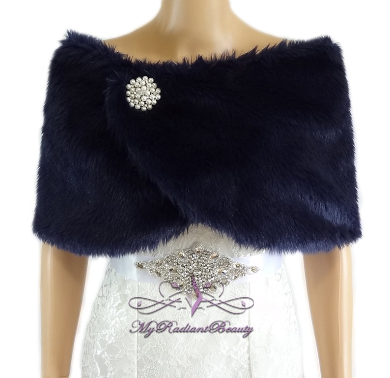 May include: Navy blue faux fur shawl with a jeweled brooch. The shawl is draped over a white dress with a beaded belt.