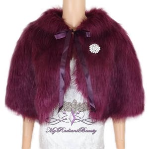 May include: A burgundy faux fur shrug with a satin ribbon tie and a jeweled brooch. The shrug is short and has a collar.