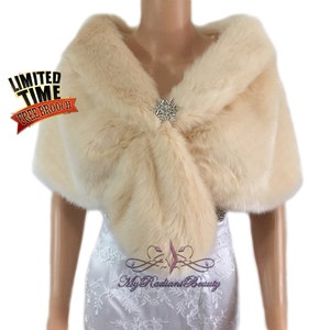 May include: A cream-colored faux fur shawl with a decorative brooch. The shawl is draped over a mannequin wearing a white dress.  Limited Time Free Brooch.