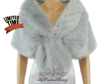May include: A silver faux fur shawl with a large, sparkly brooch in the center. The shawl is draped over a white dress.