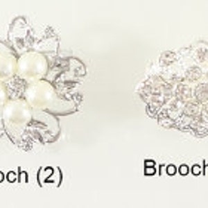 May include: Four silver brooches with intricate designs. The first brooch is a square with a floral pattern. The second brooch is a flower with five white pearls in the center. The third brooch is a round design with a floral pattern. The fourth brooch is a round design with a floral pattern.