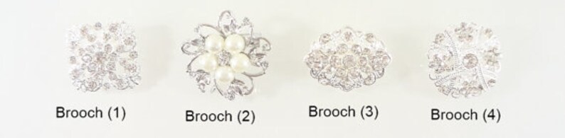 May include: Four silver brooches with intricate designs. The first brooch is a square with a floral pattern. The second brooch is a flower with five white pearls in the center. The third brooch is a round design with a floral pattern. The fourth brooch is a round design with a floral pattern.