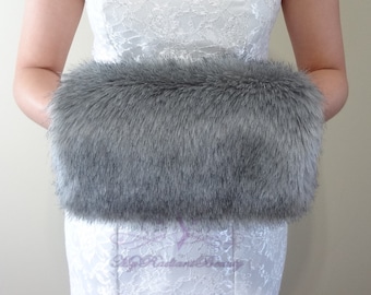 Puede incluir: Un bolso de mano de piel sintética gris. El bolso de mano está hecho de piel sintética suave y esponjosa y tiene una forma rectangular.