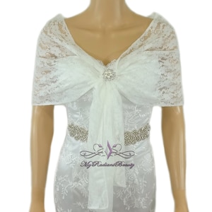 May include: White lace bridal shawl with a bow and a rhinestone brooch. The shawl is draped over a white dress with a rhinestone belt. The text "My Radiant Beauty" is visible in the bottom right corner of the image.