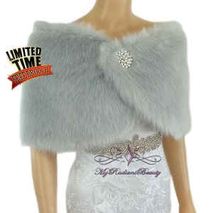 May include: A silver faux fur shawl with a rhinestone brooch. The shawl is draped over a white dress with a rhinestone belt. The text "Limited Time Free Brooch" is in the top left corner of the image.