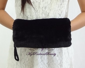 Puede incluir: Un bolso de mano de piel sintética negra con una correa de muñeca. El bolso rectangular tiene un aspecto suave y texturizado. El texto "My Radiant Beauty" está impreso en la parte inferior de la imagen.