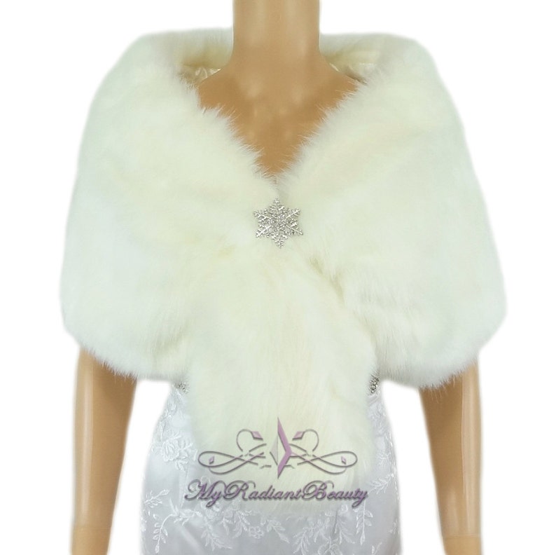 Puede incluir: Chal de piel sint&eacute;tica blanca con un broche de cristal en forma de copo de nieve. El chal est&aacute; drapeado sobre un maniqu&iacute; que lleva un vestido blanco.