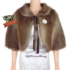 May include: A brown faux fur shrug with a satin ribbon tie and a rhinestone brooch. The shrug has a collar and short sleeves.