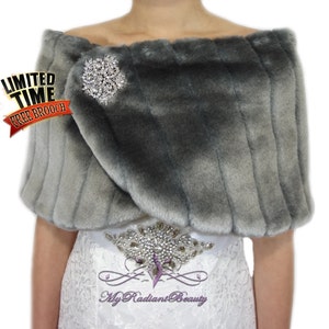 May include: A gray faux fur shawl with a silver rhinestone brooch. The shawl is draped over a white dress with a rhinestone belt. The text "Limited Time Free Brooch" is in the top left corner of the image.