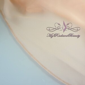May include: Close-up of a peach-colored fabric with a stitched edge. The fabric has a subtle sheen and a soft, drapey texture. The text "My Radiant Beauty" is embroidered in a light purple color on the fabric.