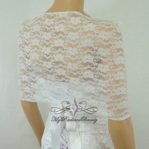 May include: White lace bridal shrug with a delicate floral pattern. The shrug is shown on a white dress with a satin ribbon.