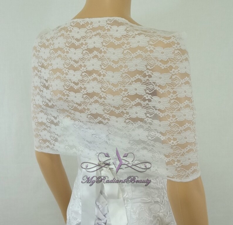 May include: White lace bridal shrug with a delicate floral pattern. The shrug is shown on a white dress with a satin ribbon.
