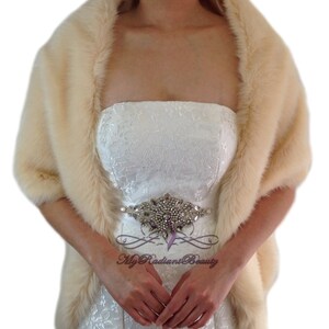 May include: A cream-colored faux fur shawl with a satin-like lining. The shawl is draped over a person's shoulders and is worn with a strapless dress.