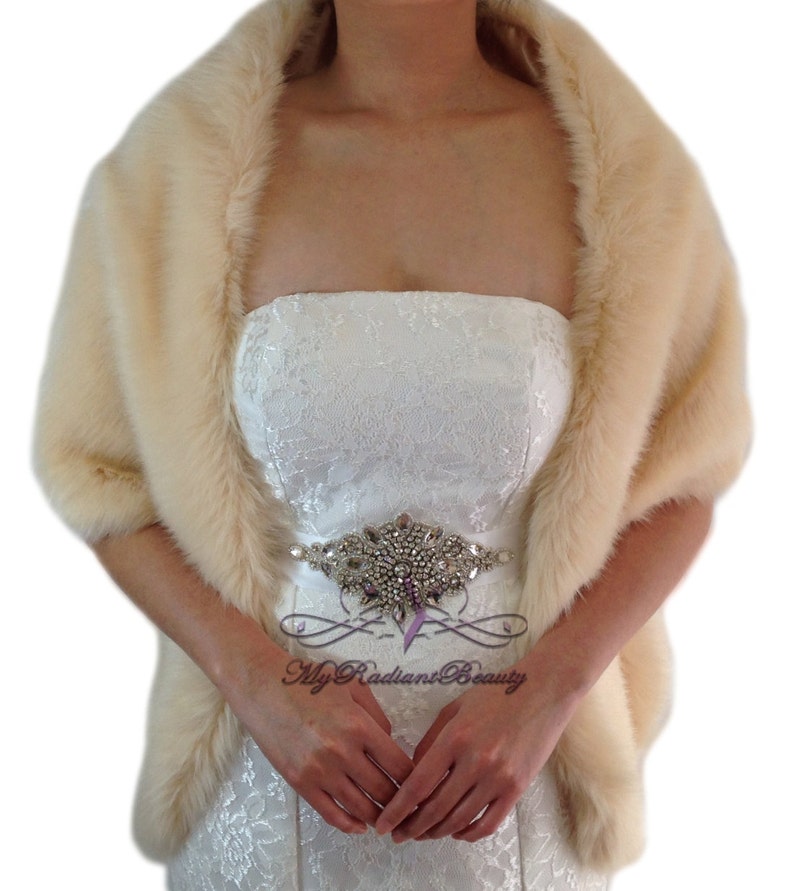May include: A cream-colored faux fur shawl with a satin-like lining. The shawl is draped over a person's shoulders and is worn with a strapless dress.