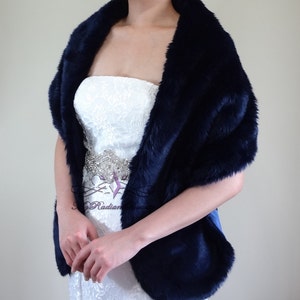May include: A navy blue faux fur shawl with a satin ribbon trim. The shawl is draped over a white strapless dress with a beaded belt.