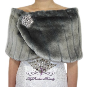 May include: Gray faux fur shawl with a silver rhinestone brooch. The shawl is draped over a white dress with a rhinestone belt.