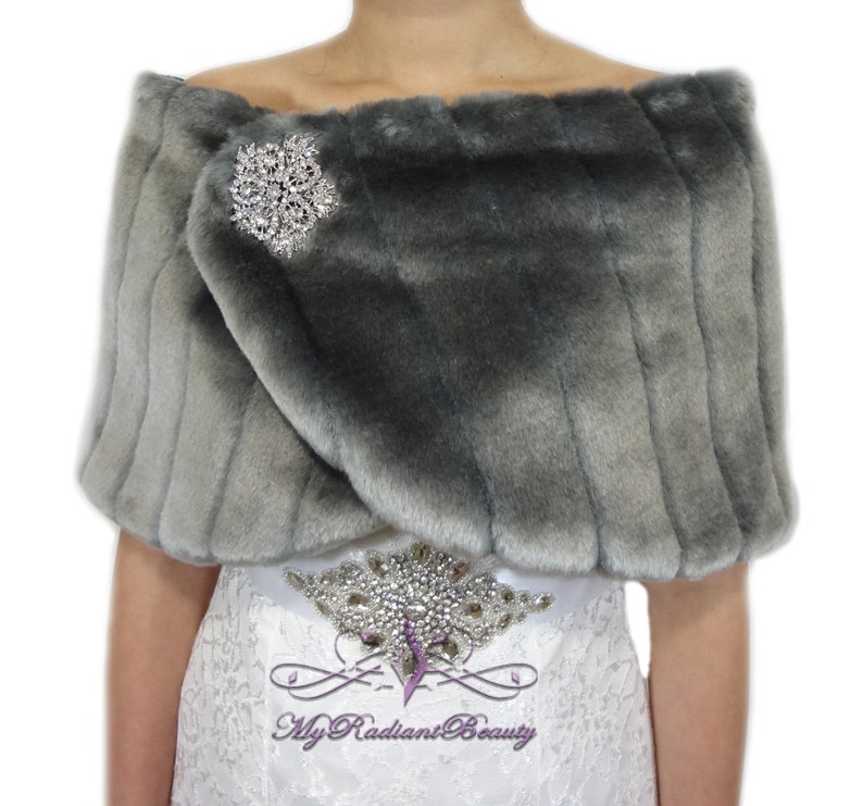May include: Gray faux fur shawl with a silver rhinestone brooch. The shawl is draped over a white dress with a rhinestone belt.
