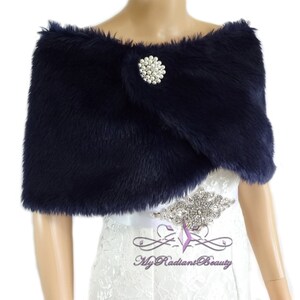 May include: Navy blue faux fur shawl with a pearl and rhinestone brooch. The shawl is draped over a white dress.