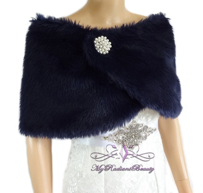 May include: Navy blue faux fur shawl with a pearl and rhinestone brooch. The shawl is draped over a white dress.