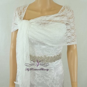 May include: White lace bridal shawl with a delicate floral pattern. The shawl is draped over a mannequin's shoulders and tied at the neck. The shawl is made of soft, sheer lace and would be a beautiful addition to any bridal ensemble.