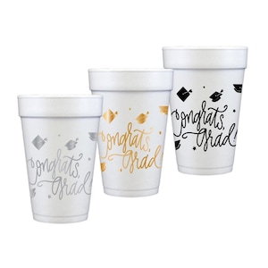Puede incluir: Tres vasos de espuma blancos con dise&ntilde;os de graduaci&oacute;n. Uno tiene detalles plateados, otro dorados y el tercero negros. Todos los vasos presentan el texto "Congrats Grad" en una fuente cursiva, junto con gr&aacute;ficos de gorro de graduaci&oacute;n y estrellas.
