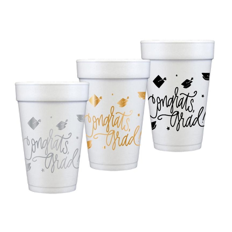 Puede incluir: Tres vasos de espuma blancos con dise&ntilde;os de graduaci&oacute;n. Uno tiene detalles plateados, otro dorados y el tercero negros. Todos los vasos presentan el texto "Congrats Grad" en una fuente cursiva, junto con gr&aacute;ficos de gorro de graduaci&oacute;n y estrellas.