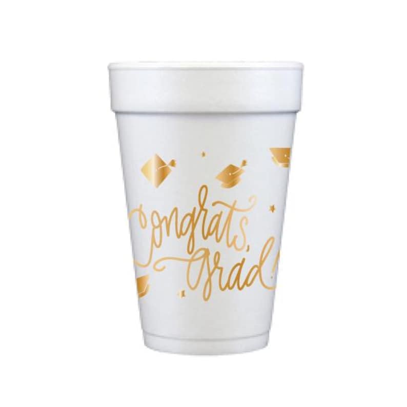 Puede incluir: Vaso de espuma blanco con letras doradas y gr&aacute;ficos de gorros de graduaci&oacute;n. La taza dice "congrats grad!" en una fuente cursiva. La taza est&aacute; dise&ntilde;ada para una celebraci&oacute;n de graduaci&oacute;n.