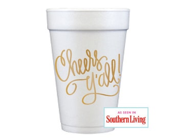 Puede incluir: Vaso de espuma blanco con letras doradas que dicen "Cheers y'all!" y un logotipo rojo y blanco que dice "As seen in Southern Living".